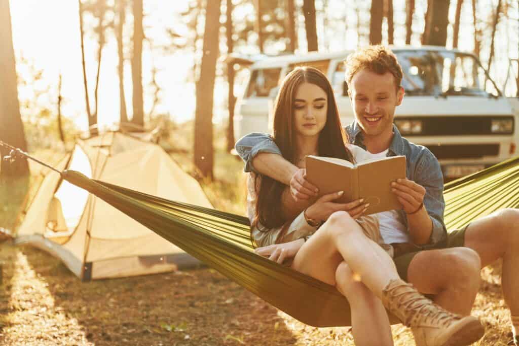 Holding book. Young couple is traveling in the forest at daytime together