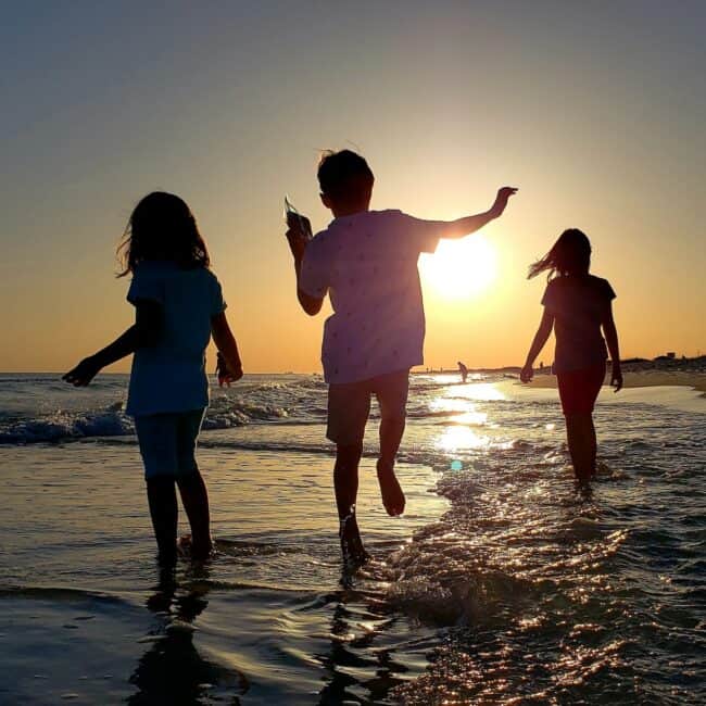 Silhouetted kids walking in the ocean at sunset having fun during the golden hour at sea.