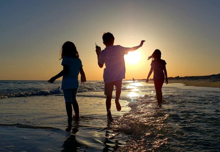 Silhouetted kids walking in the ocean at sunset having fun during the golden hour at sea.