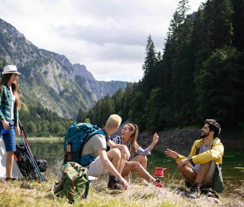 Smiling young people enjoying nature beside tents and talking outdoor