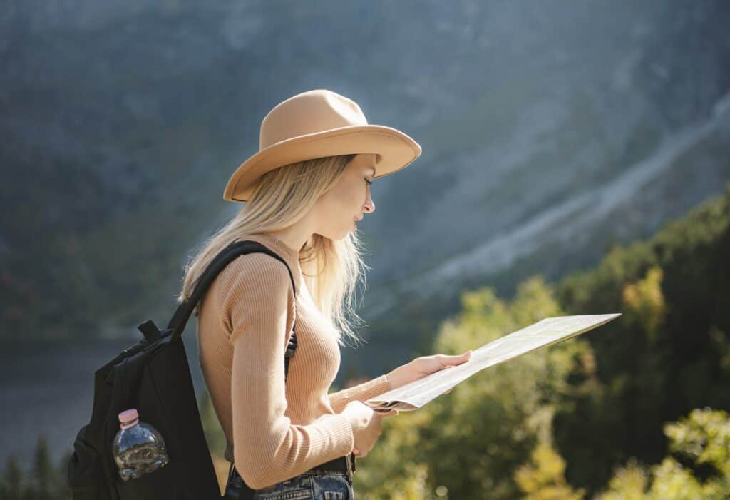 Wanderlust and travel concept. Stylish traveler girl in hat looking at map, exploring woods.