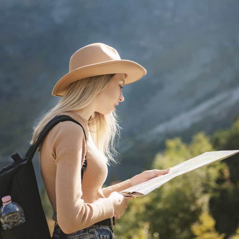 Wanderlust and travel concept. Stylish traveler girl in hat looking at map, exploring woods.